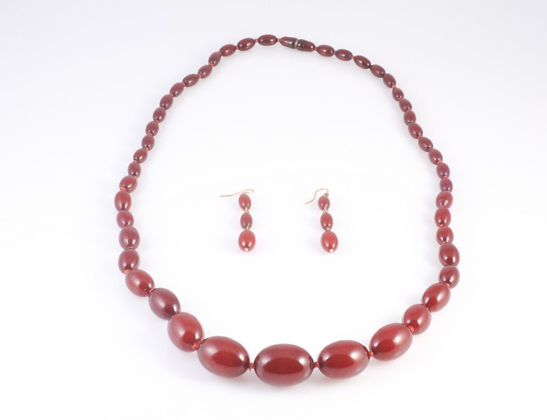 AN AMBER COLOURED BEAD NECKLACE, the forty five: AN AMBER COLOURED BEAD NECKLACE, the forty five graduating oval beads each strung knotted onto a screw barrel clasp. Total length 76cm. Weight 62.9gms; and a pair of earrings to match, the three gradu