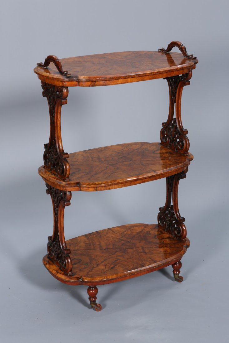 A VICTORIAN BURR WALNUT ETAGERE, CIRCA 1860-70, the: A VICTORIAN BURR WALNUT ETAGERE, CIRCA 1860-70, the three shaped oval tiers with moulded edge and quarter veneers, supported by fret carved pillar ends, raised on turned legs moving on castors. 106cm 