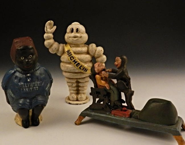 Grouping of Vintage Cast Iron Banks: Michelin cast iron standing tire man, measures: 8 1/2 inches Dentist pulling teeth cast iron bank, measures: 5 x 8 1/2 inches Laxative cast iron bank, measures: 7 x 4 inches