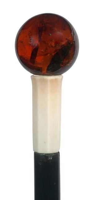 219. Amber Dress Cane-Early 20th Century-An amber: 219. Amber Dress Cane-Early 20th Century-An amber sphere with various objects within, carved ivory collar, ebony shaft and no ferrule. H. 1 ¾" x 1 ¾", O.L. 34 ½", $500-$1000
