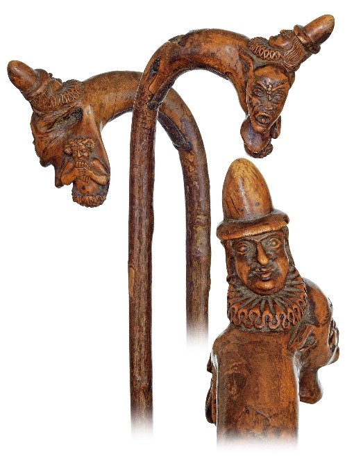 53. Folk Art Cane-Ca. 1850-Fashioned of a single branch: 53. Folk Art Cane-Ca. 1850-Fashioned of a single branch with a natural bough carved with two different Pan heads topped by a clown portrait with frilled collar and bonnet. 4 ¾” long iron ferrule. I