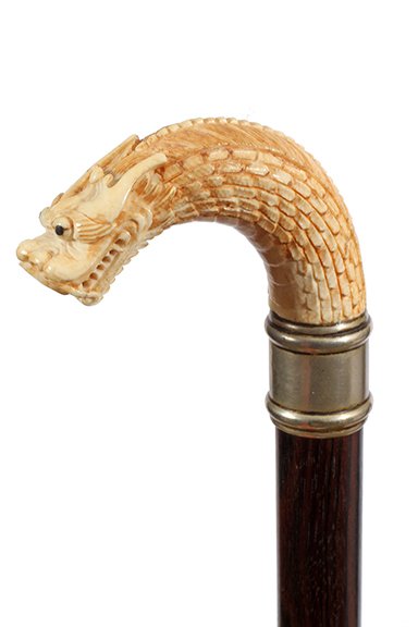 Dragon Dress Cane: Ca. 1900-A carved dragon done in high relief with beaded eyes, nickle silver collar, exotic hardwood shaft and a metal ferrule. H- 2" x 3" O.L.- 35"
