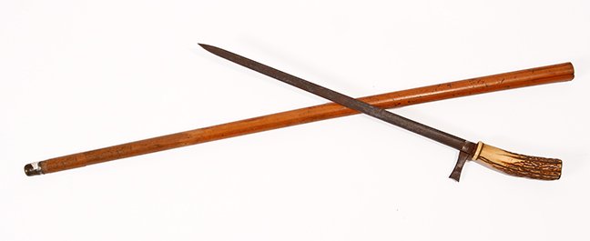 49. Stag Sword Cane- Ca. 1830- A stag handle with a: 49. Stag Sword Cane- Ca. 1830- A stag handle with a brass disc atop, blade has one hilt which folds out, malacca shaft, metal ferrule, two-sided 15 ¾” blade with push pull mechanism. H.- 4 ¼” x 