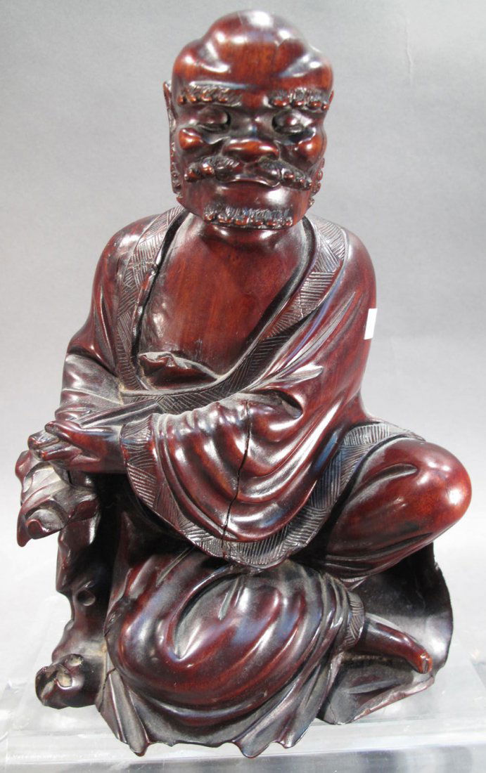 ASIAN WOOD CARVED FIGURINE. Old man sitting: ASIAN WOOD CARVED FIGURINE. Old man sitting crossed-legged holding his flute with eyes closed. 10 1/2"h. (Note: crack down left arm).