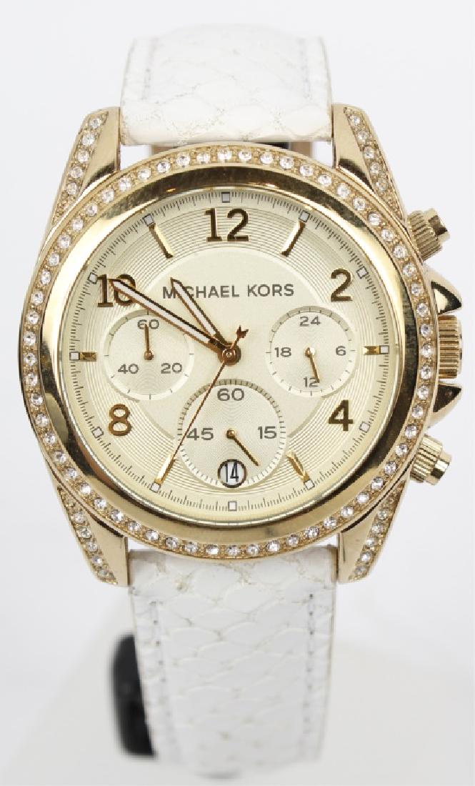 MICHAEL KORS LADIES GOLD TONE WHITE LEATHER WATCH: MICHAEL KORS LADIES GOLD TONE WHITE LEATHER WATCH Gold plated stainless steel case with a white leather strap. Gold tone stainless steel bezel set with Swarovski crystals. Champagne dial with gold-ton