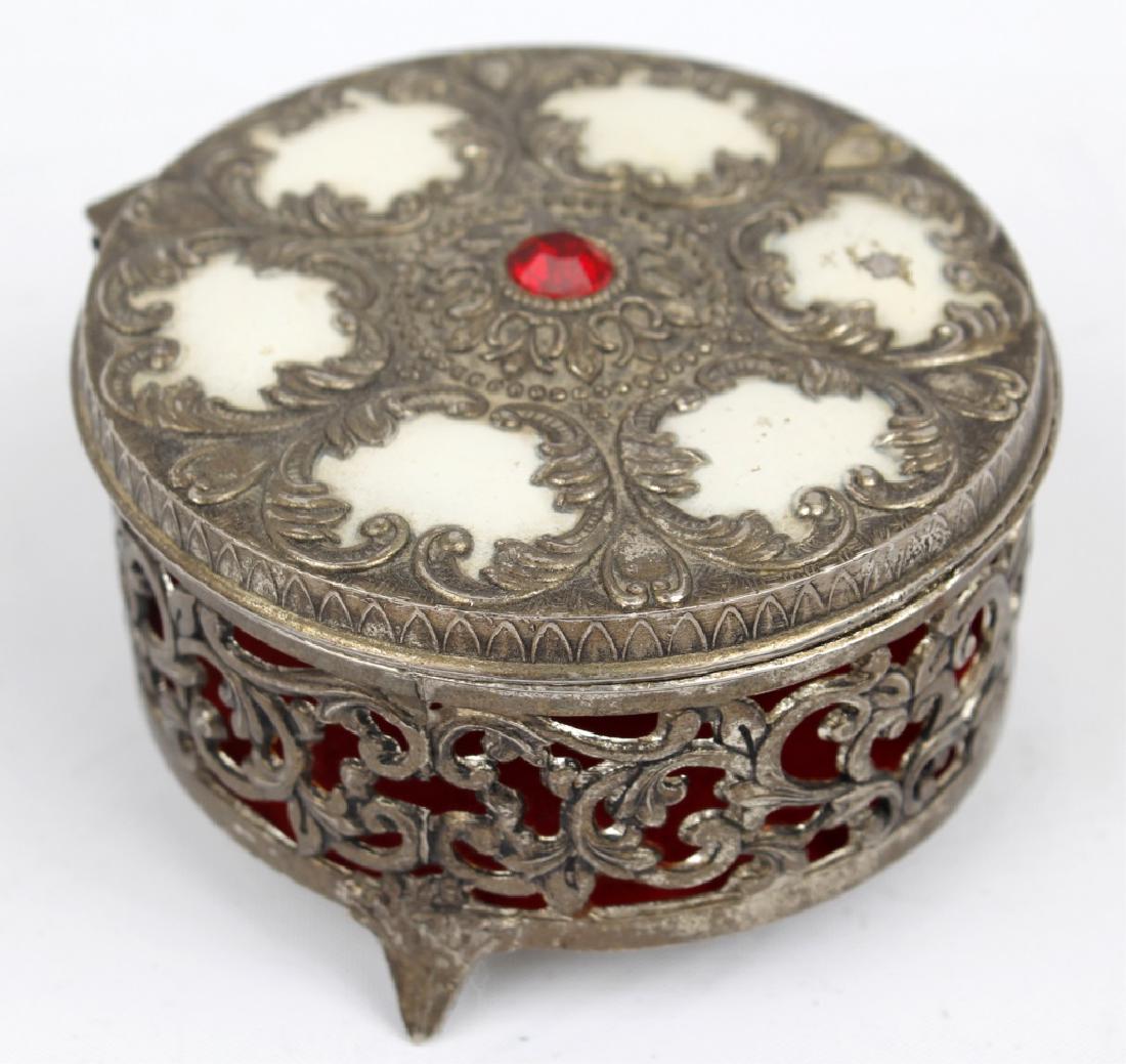 VINTAGE METAL JEWELRY BOX: VINTAGE METAL JEWELRY BOX Vintage metal jewelry box with white enamel detail and a red rhinestone. Red velvet interior with 3 pedestal feet. 3.25" diameter x 1.75" H