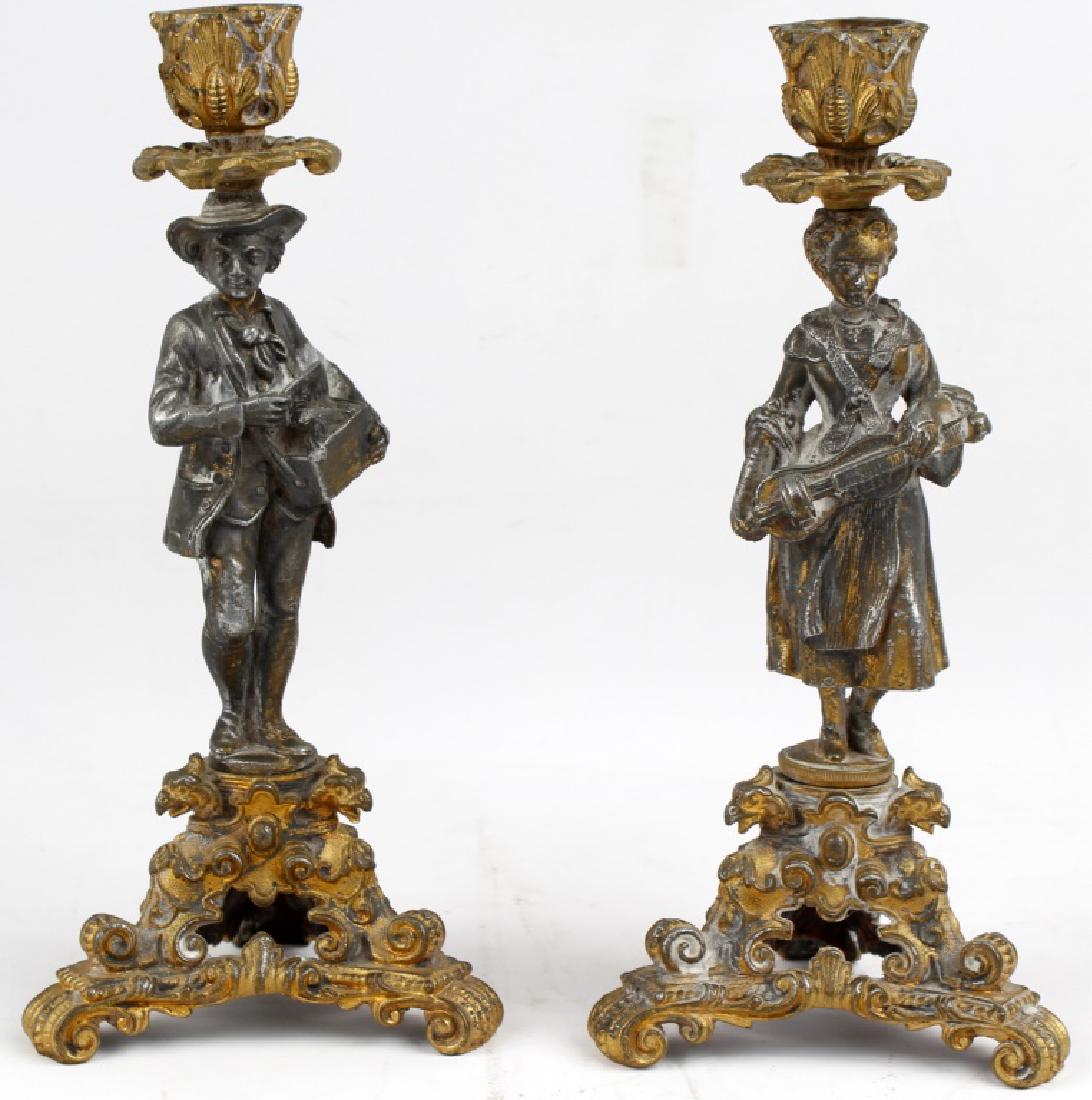 FRENCH FIGURAL CANDLESTICK CAST WHITE METAL: FRENCH FIGURAL CANDLESTICK CAST WHITE METAL French figural street act candlestick holders in cast white metal with a fading gold tone finish. (1) French maiden with a violin, (1) French man with a box