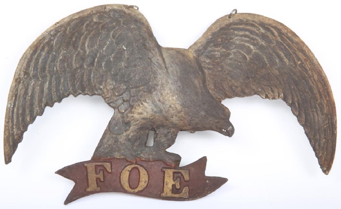 FRATERNAL ORDER OF EAGLES CAST METAL SIGN FOE: FRATERNAL ORDER OF EAGLES CAST METAL SIGN FOE Cast metal sign depicting a perched eagle on a banner that reads "FOE", reverse marked Foster Stove Foundry c. 1908. Size: 15 x 9"