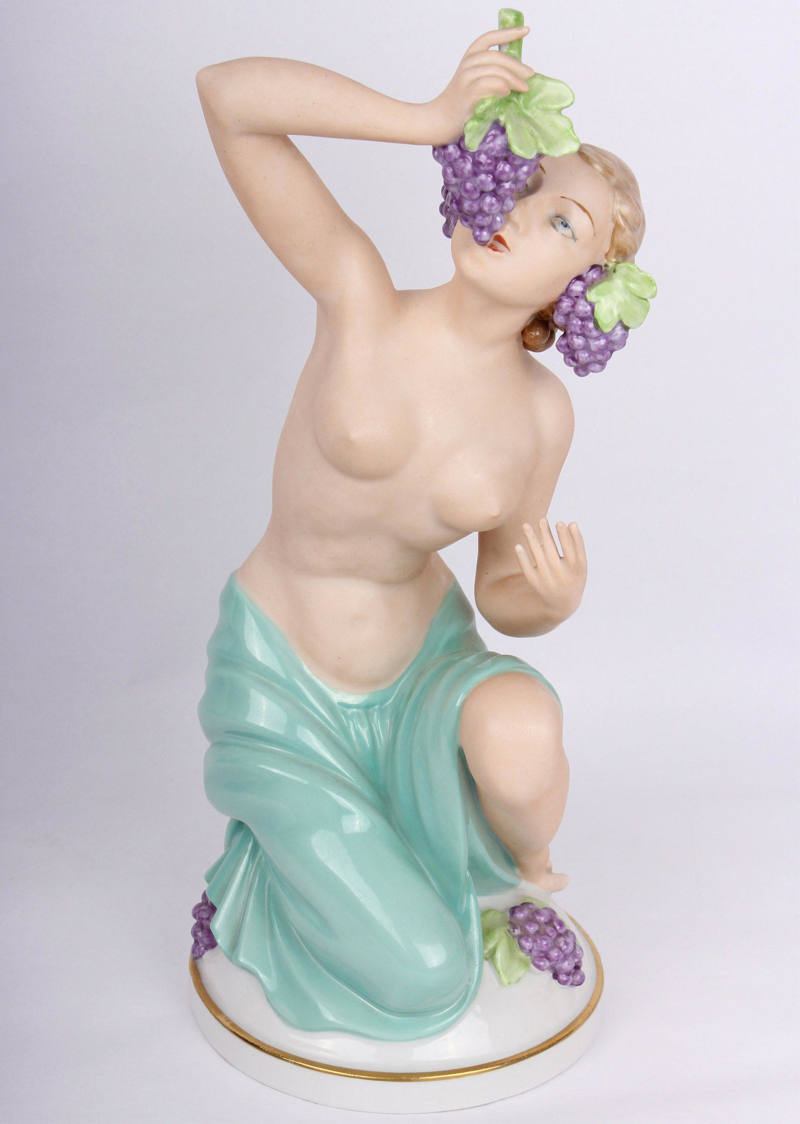 GERMAN PORCELAIN NUDE FEMALE STATUE EATING GRAPES: GERMAN PORCELAIN NUDE FEMALE STATUE EATING GRAPES Porcelain partially nude female statue kneeling while eating grapes on a white and gold gilt base. Underside simply marked "Germany" in gold lettering