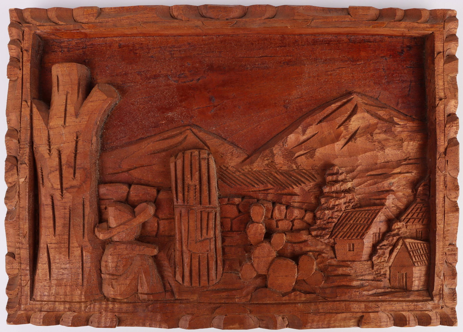 WOODEN PUEBLO DESERT COWBOY RELIEF CARVING: 139180 WOODEN PUEBLO DESERT COWBOY RELIEF CARVING Carved relief wooden art piece of cowboy sitting against tree, with cactus, town and mountain desert landscape. Size: 15 X 11"Condition: Refer to imag