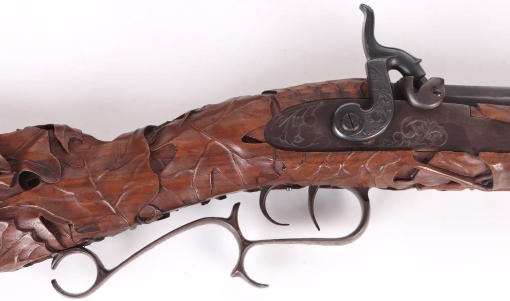 THOMPSON .50 CAL. RENEGADE W/ DEEP RELIEF DESIGN: Thompson .50 Cal. Center Renegade with a wooden ramrod. Rifle is sleek and displays deep relief design from the stock to the fore body. Design looks rich and detailed. Rifle comes with carrying case.