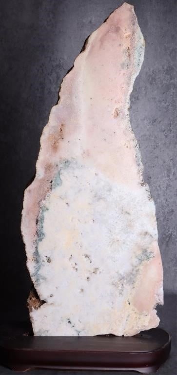 ROSE AMETHYST GEODE SLAB 2.5FT TALL BRILLIANT: Rose amethyst geode slab stood on a wood base. The surface is pockmarked with crystal clusters and the overall stone features a variety of colors and textures. 32" x 14" X 1.25" slab, 2" X 18" X 8" ba