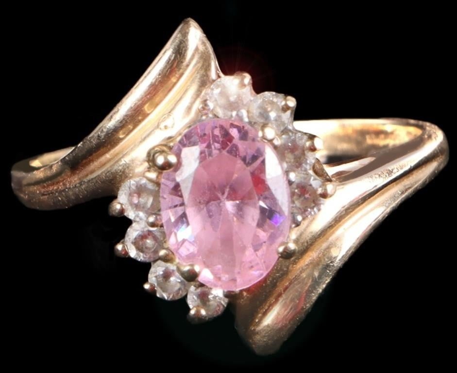 10K YELLOW GOLD SWIRL STYLE LADIES RING: 10K yellow gold swirl style ladies ring. This ring features an oval cut pink rhinestone with a halo of white rhinestones in a bypass or swirl- style band where the gold splits to hold the center stone