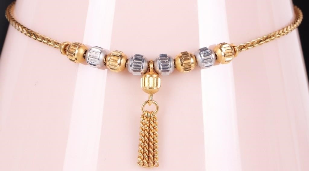 22K YELLOW GOLD LADIES BRACELET W/ BEADS & CHARM: 22k yellow gold ladies bracelet. The face features an alternating pattern of yellow and white gold beads. A single bead projecting off the center with a chain tassel dangling from it. A heart charm