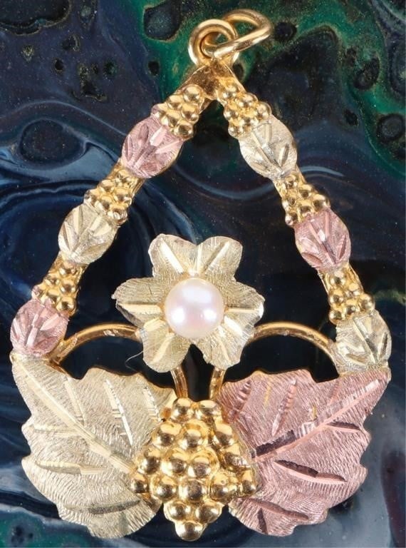 10-12K LADIES PENDANT GRAPES LEAVES BLACK HILLS: 10-12k yellow gold ladies pendant by Black Hills Gold. The piece is an elongated and inverted diamond shape with saturated green and purple-tone leaves with gold-tone bunches of grapes. In the center 