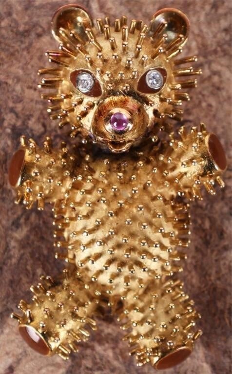 18K YELLOW GOLD TEDDY BEAR PENDANT W/ DIAS & RUBY: 18K yellow gold teddy bear pendant. The surface is covered in filaments designed to make the bear appear fuzzy. The paws are colored with brown enamel. The eyes are two 0.05ct round-cut diamonds and t