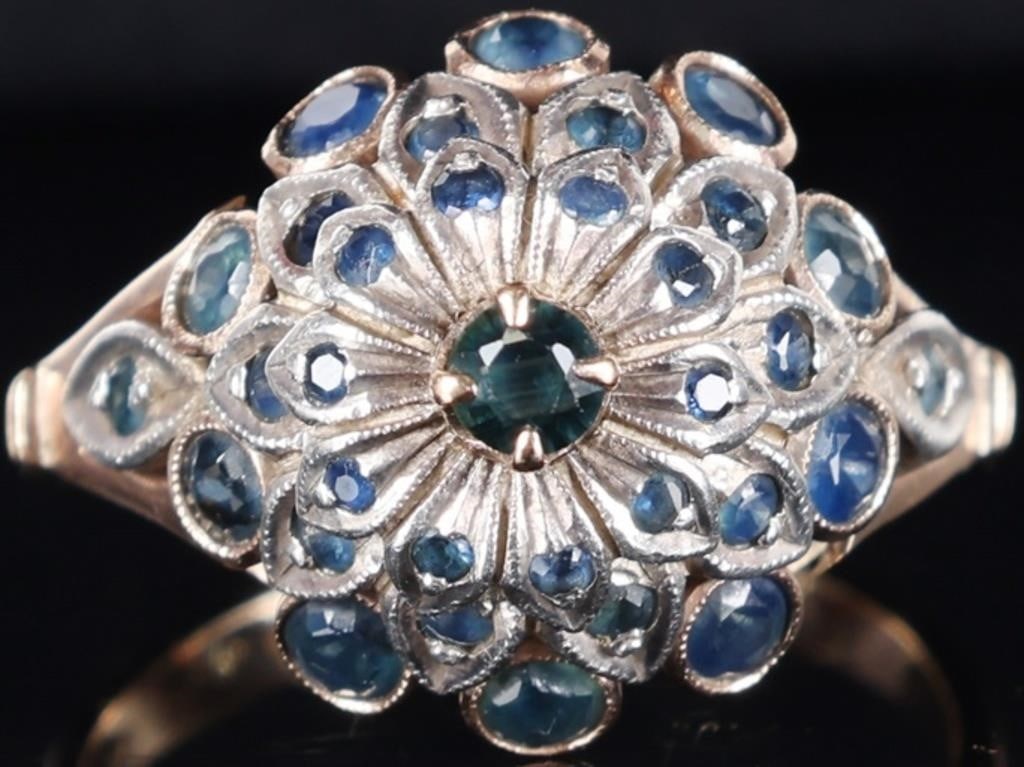 8K YELLOW/WHITE GOLD LADIES FLORAL RING W SAPPHIRE: Vintage 8k gold ladies ring with an elaborate floral pattern on the face and encrusted with thirty-three round-cut blue sapphires (1.12ctw). The center stone is a 0.1ct piece. Beneath it is a white go