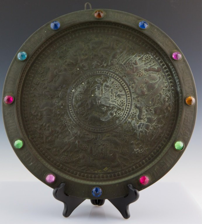 CIRCULAR COPPER REPOUSSE WALL MEDALLION: CIRCULAR COPPER REPOUSSE WALL MEDALLION Circular copper repousse wall medallion with faceted, colored glass set into the outer rim. Imagery consists of stylized animals and men riding horses. Size: 14