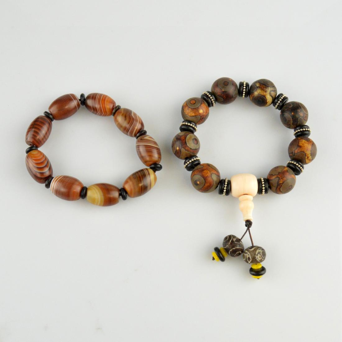 Dzi Bead Bracelet Pair: 天珠手串兩個 2 Item Lot; a pair of differing dzi bead bracelets. One with circular beads; one 'silk' or 'striped' rounded barrel beads.