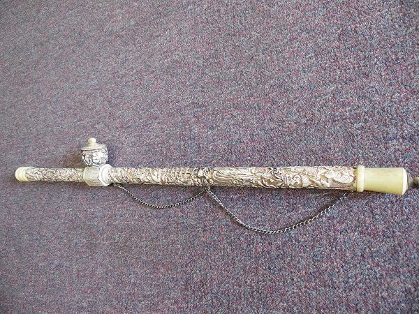 A Vintage Carved Bone Opium Pipe: An Old Bone Opium pipe with intricately carved motif such as Birds, Flowers, Pagoda, Trees and Luckily Kids. Opium Pipe has a Metal Chain as a handle. Size: L 50cm, D 4.5cm.
