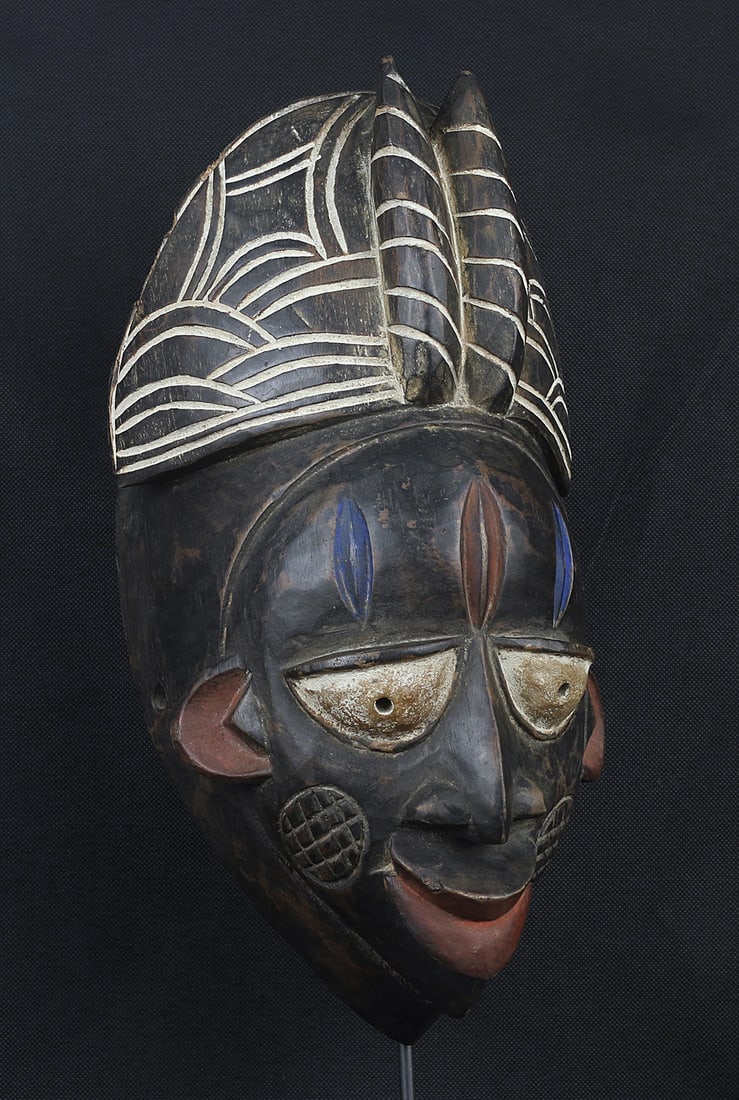 Nigeria 1970 Igbo Wooden mask 37cm: Nigeria. 1970 circa. Igbo People. Wooden mask decorated, wooden crown on the top. Black, Blue and red pigmentation. 960 gr. - 37x20x16cm