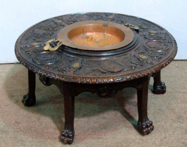 ANTIQUE EUROPEAN WOODEN HAND CARVED FIGURAL TABLE: Antique European Wooden hand Carved figural table. Has profiles of military men's faces. Has carved dragons, weapons & armor. Has a metal bowl that can be removed in the center. 18" H x 38" diameter.