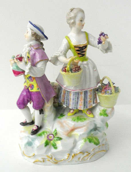 MEISSEN HAND PAINTED TWO FIGURE PORCELAIN GROUP: Meissen hand painted two figure porcelain group of a young man dressed in purple outfit with yellow-white frills & black shoes and a young lady with a blue & rust colored skirt. Carrying two baskets f