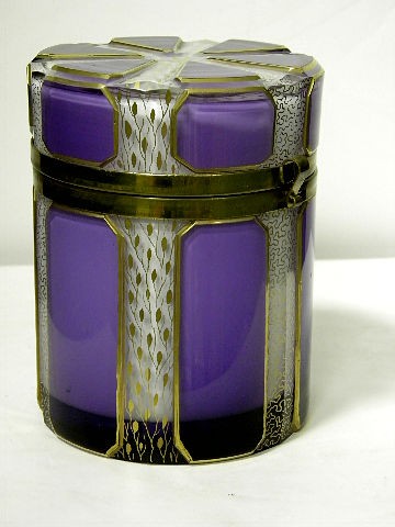 Gilt metal mounted Amethyst and opaline glass Jar: TAmethyst and opaline glass covered jar has gilded amethyst colored glass panels. The hinged top opening reveals a chyclindrical white opaline glass interior. Measures 5" high and 4" diameter. Shippin