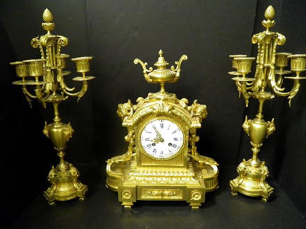 Large Anique Dore Bronze Clock Garniture: A large antique dore bronze clock garniture. The clock having a white porcelain dial,. The bell striking movement stamped: Medalle De` Argent, Vencenti 1855. The clock case, and candelabra decorated w