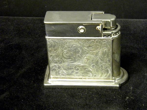 A large sterling silver table lighter: A large sterling silver table lighter bearing the inscription Ursula & Dave, Frankfurt A.M. 26th Nov 1953. The silver decorated both sides and stamped 935. The mechanism is operated by depressing a bu