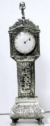 Antique Dutch Sterling Minature Long Case: An antique Sterling Silver model of a typical 18c Dutch Grandfater Clock housing a pocket watch movement.The case decorated with hunting scenes, Windmills, and a Barge. The back of the model having a 