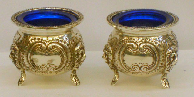 Hand Chased Sterling Repousse Pair of Salt Cellars: Set of 2 footed, hand chased sterling silver repousse salt cellars. Both salt cellers have a English Victorian floral design with lion heads at the base of the legs and have blue glass inserts. Bottom