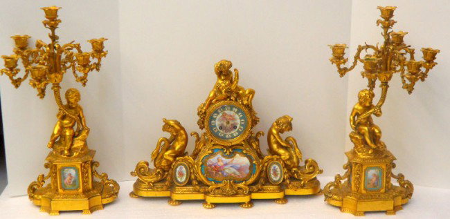 Antique Sevres Dore Bronze & Porcelain Clock Set: Antique Sevres Dore Bronze & Porcelain three piece clock set having Sevres plaques on face of clock, bottom plaques throughout, and candelabras have great detail. Measures , clock - 14 1/2" high x 20 