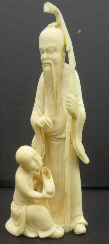 Carved Ivory Figure of a Man and Servant: Handsome carving of a man and his servant carved in exquisite fine detail. The man has a long flowing robe and beard and has a staff in his hand. The servant appears to be putting a shoe on the man. T
