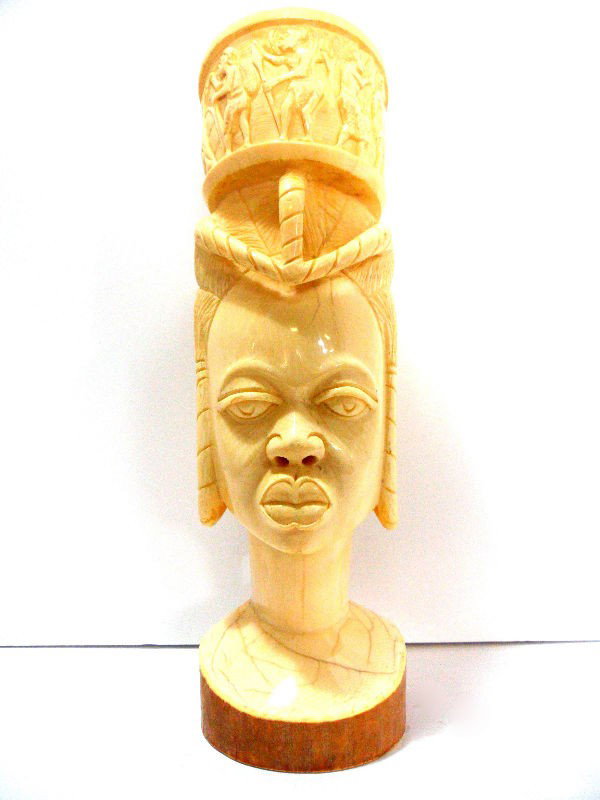 African Ivory Carved Head of a Woman: An African ivory carved head of a woman. She is carrying a water basket atop her head, which serves as a container with a lid. The basket is beautifully carved with a frieze of African warriors. The w