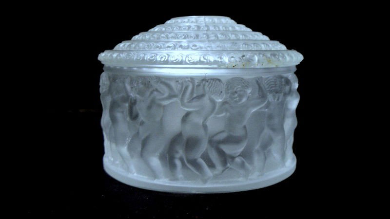 Lalique Carved Round Box with Lid: Lalique round box with Lid. Base of the box contains a frieze of young male figures holding up the lid. The lid is carved with concentric circles patterned with rosettes. Bottom is signed "Lalique." D