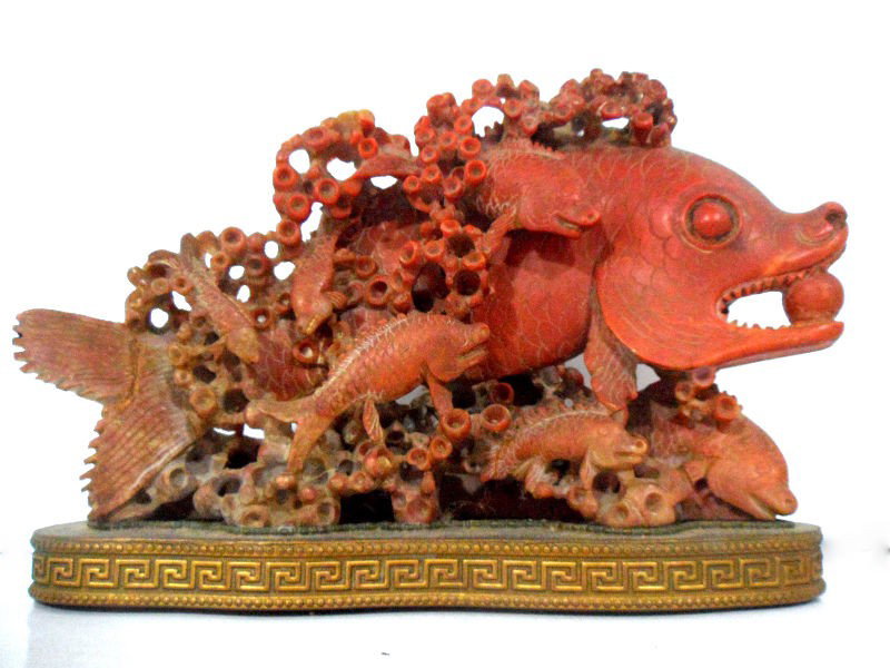 Chinese Soapstone Carving of a Fish: Chinese soapstone carving of a fish. A large fish holding a ball in its mouth has been carved with six smaller fish swimming around it. Sea plants surround all the fish. The sandstone is in a maroon c
