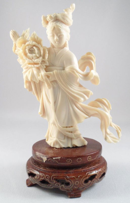 Chinese Ivory Figure of a Flowing Beauty: Chinese ivory figure of a flowing beauty. The figure is fluidly carved with robes that appear to be blowing in the wind. She holds a large flower in her hands and wears an elaborate hair style. Piece