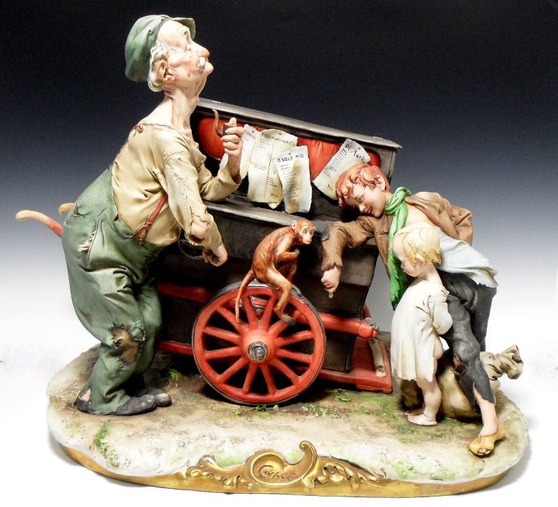 Capodimonte Porcelain Organ Grinder Music Box: Capodimonte porcelain organ grinder music box. The organ grinder stands, cranking his organ while his monkey and two young tramps look on. The organ winds up to produce music. The piece is signed "Org