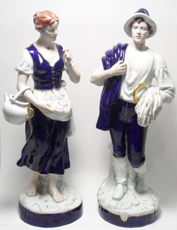 Royal Dux Porcelain Figures of Peasants (2): Pair of Royal Dux porcelain figures of peasants. The female figure holds a large vessel and her apron is filled with apples; the male figure holds a sickle and wheat in one hand and his cape in the ot