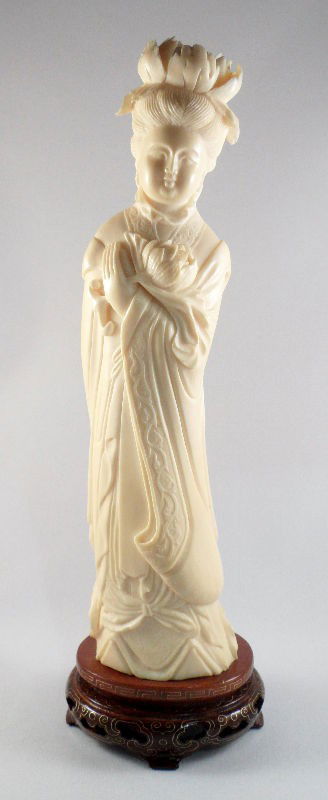 Chinese Ivory Figure of a Floral Beauty: Chinese ivory figure of a floral beauty. The figure has a large chrysanthemum headdress and holds a bloom in her hand. Her long robes flow to the ground, and they are etched with scroll work designs.