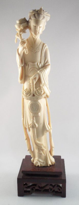 Chinese Ivory Figure of a Floral Beauty: Chinese ivory figure of a floral beauty. She wears a phoenix headdress and holds a rose in one hand and a basket of flowers in the other. Her robes are beautifully detailed. Piece stands atop a carved