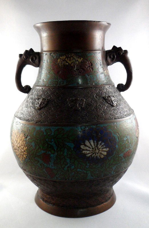 Chinese Cloisonné Urn: Chinese cloisonné urn. Decorated with two cloisonné bands features floral images. The bronze is covered with animal heads and a geometric pattern. Measures 10"H. Shipping within the continental US i