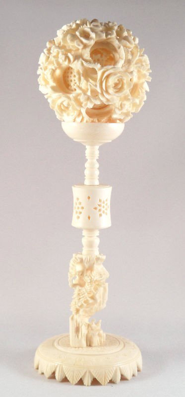 Chinese Carved Ivory Puzzle Ball on Stand: Chinese carved ivory puzzle ball on stand. The puzzle ball is ornately carved with floral designs. The stand is supported by a carved house, which is attached to a delicately carved base. Measures 8 1