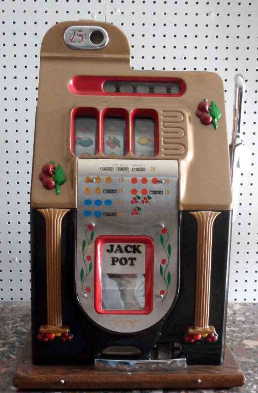 Vintage Slot Machine: Vintage slot machine. The piece is a $.25 machine operated by polling a silver metal handle. The body of the machine is in gold and it stands atop an attached wood base. Measures 25" X 15" X 16". For 