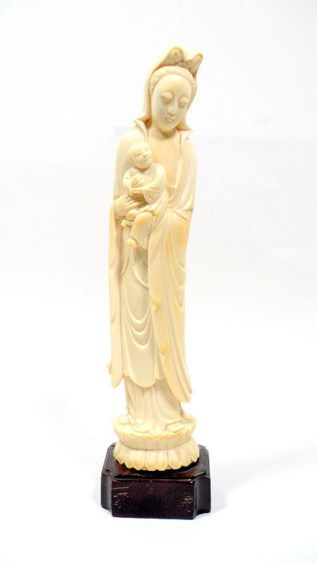 Chinese Ivory Carved Quan Yin: Chinese ivory carved Quan Yin. The female figure wears a long flowing cloak with a hood pulled up over her hair. She holds a small child who is grasping onto an object. The figure stands atop a lotus