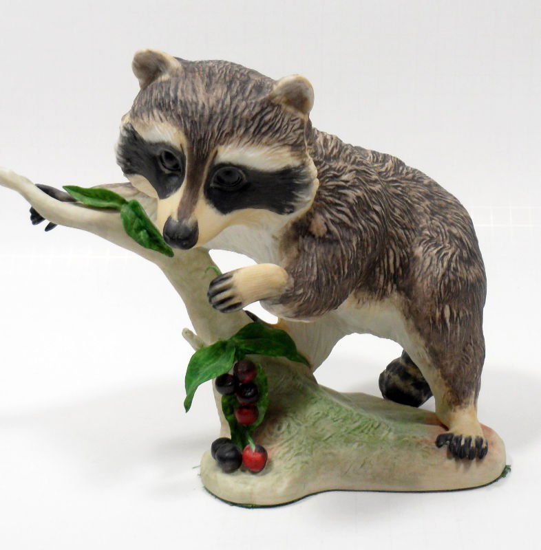 Cybis Porcelain Racoon Figure": Cybis porcelain figue of a racoon eating berries off of a brancch on a tree trunk. Very good condition, measures 7 inches height x 8 inches x 5 inches.