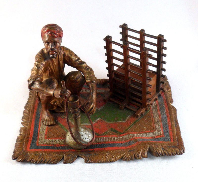 Vienna Bronze Figurine with Hookah: Vienna Bronze figurine of a Middle Eastern man smoking a hookah. The figure sits on an elaborately decorated polychrome carpet. Vienna Bronze marks are present on the bottom. Measures 3 1/2" X 4" X 5
