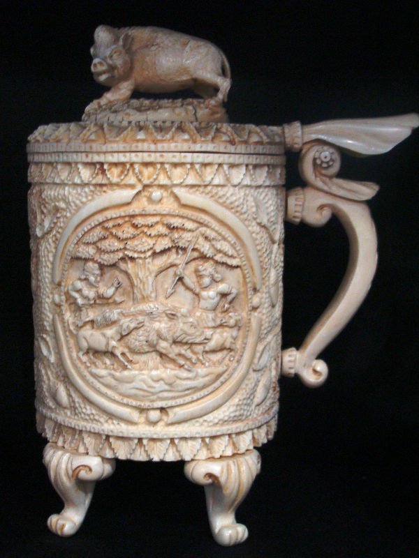 Continental Hand Carved Ivory Figural Tankard: Continental hand carved ivoryfigural footed tankard with handle. Has a barr figure as its finial and a hunting scene on one side of tankard with a boars head on the oterher side. Measures 10" heigh, 7