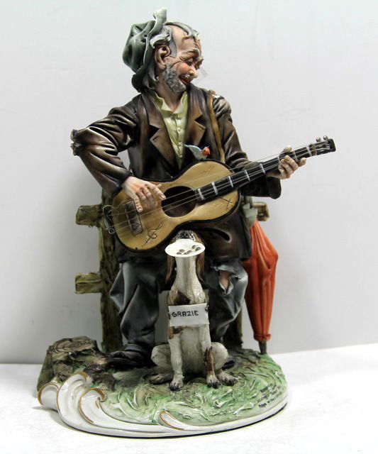 Capodimonte Italian Porcelain Figure: Capodimonte italian porcelain figure of an old man playing a guitar, having a dog sitting in front of him with a tray begging for money. measures 10 1/2" high x 6 1/2" in diameter.For Domestic or Inte